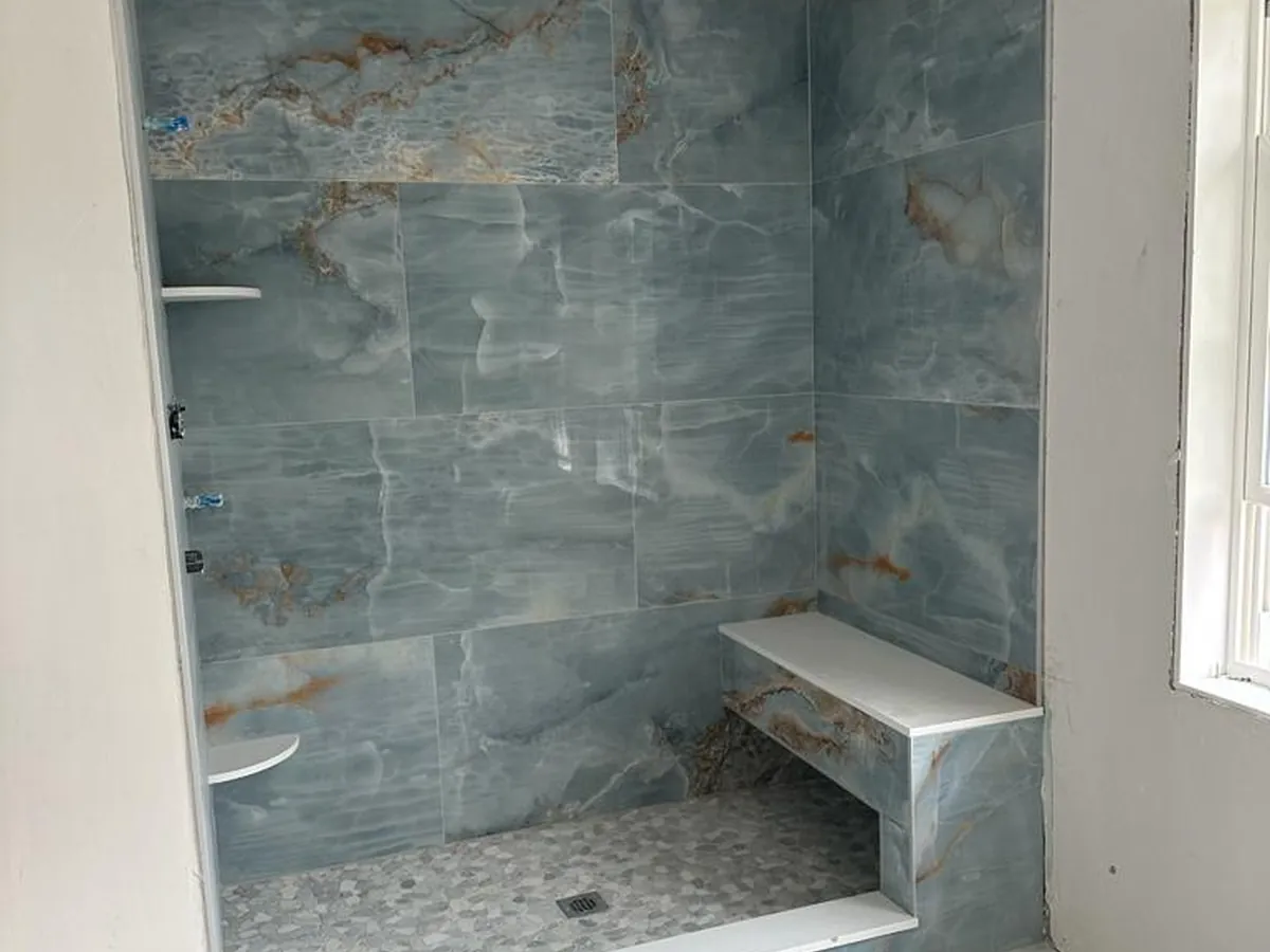 Blue marble-look porcelain shower with a tiled bench and pebble floor
